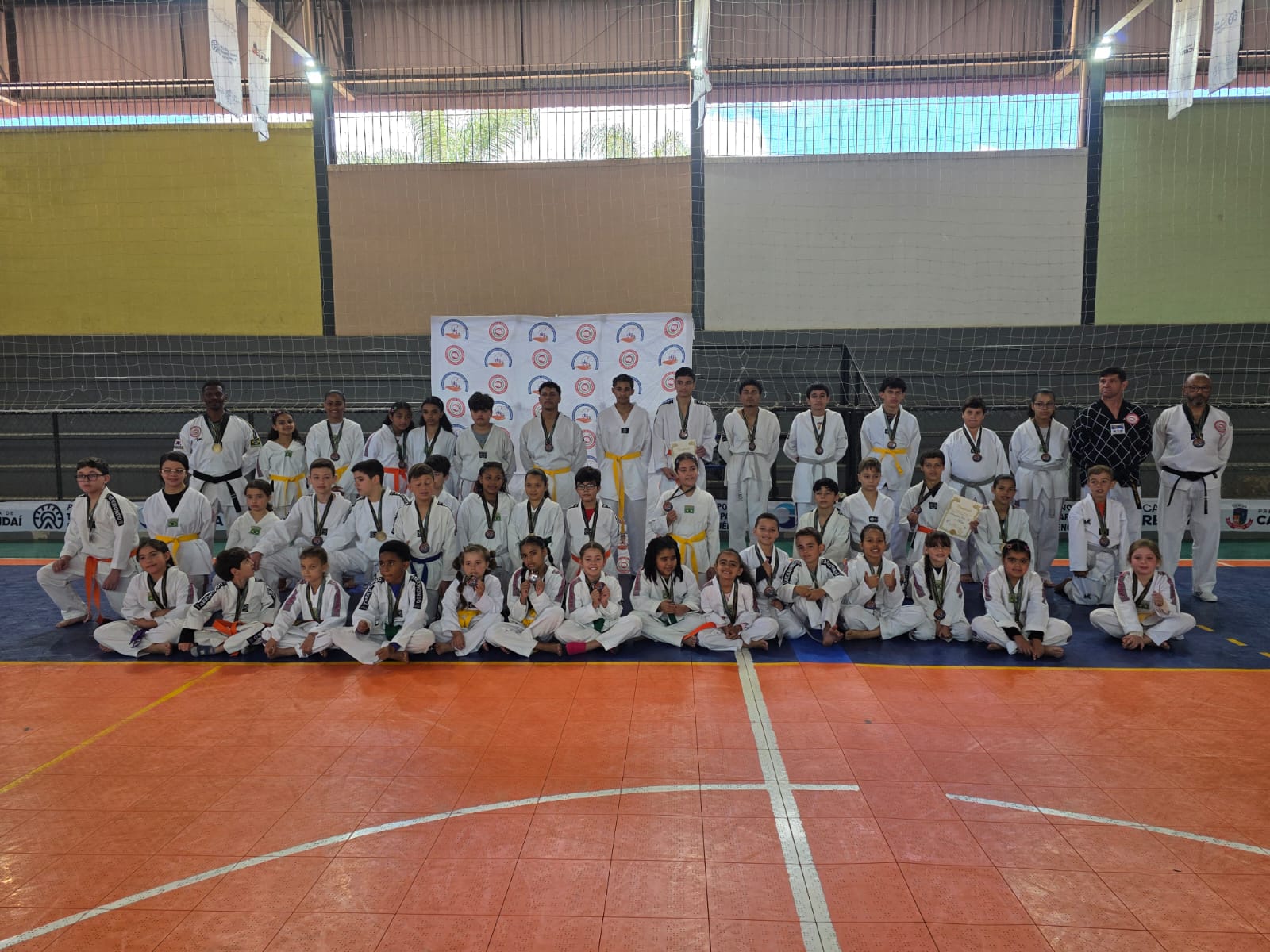 Grupo de alunos e professores do projeto com medalhas no ginásio