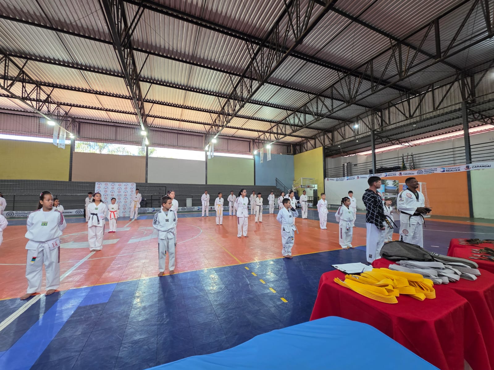 Alunos alinhados no ginásio com faixas sobre a mesa