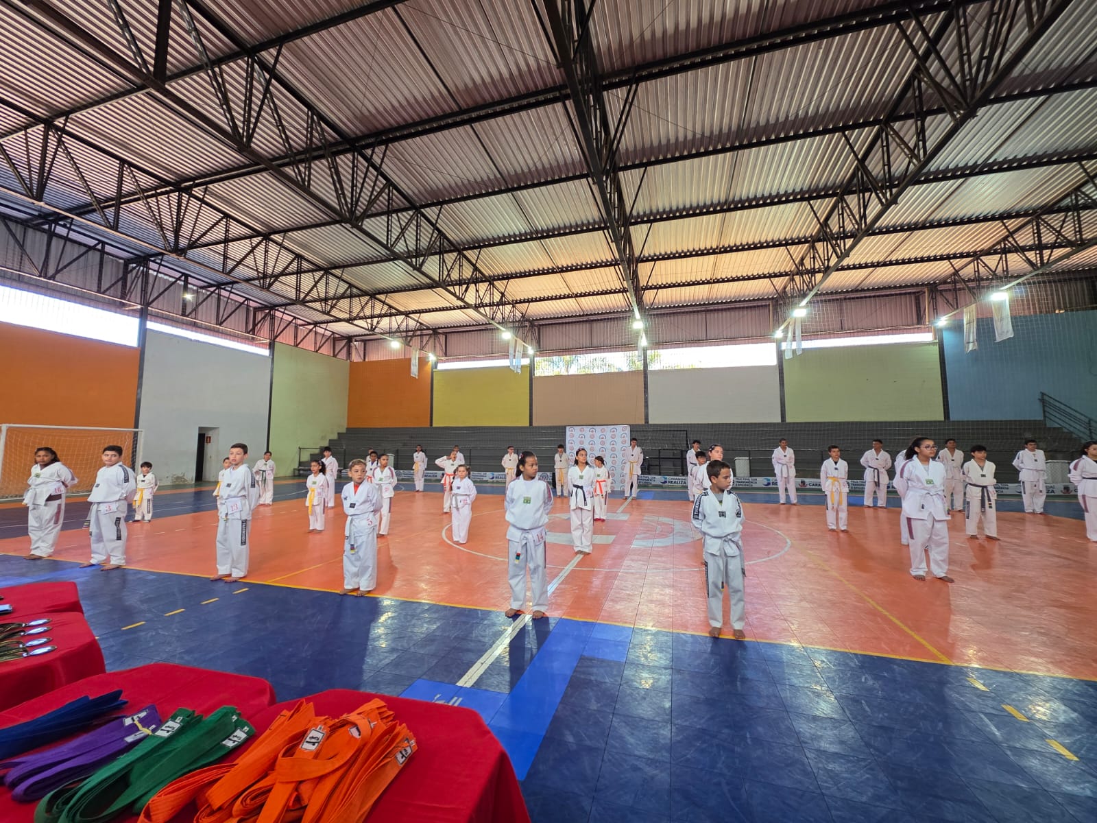 Alunos em formação no ginásio, com faixas sobre a mesa
